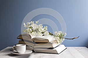 A branch of a blossoming apple tree or cherry on an open book and cup of coffee on a background of a blue wall. Concept - online