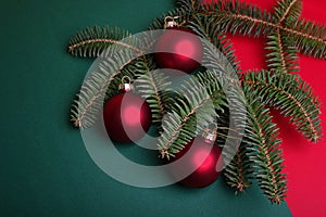 A branch of blue spruce with red christmas balls on a red and green background.