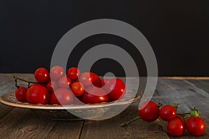 branch and bowl of small red ripe tomato closeup on wooden backg