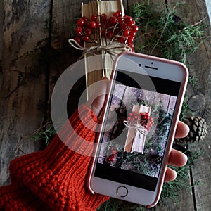 A woman photographs a book with viburnum and spruce branches from a smartphone,