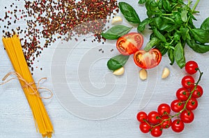 Branch of cherry tomatoes, basil, garlic, various pepper and uncooked pasta on the gray background. Top view with copy space
