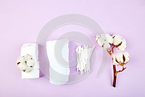Branch of cotton plant, eared sticks, cotton pads, towel, cosmetic makeup removers tampons, hygienic sanitary swabs on purple
