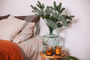 Branch fir tree at glass big vase. Cozy room decor for christmas with bed and vase with branches pine on wooden table. Hygge Xmas