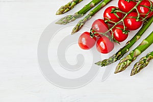 A branch of fresh cherry tomatoes and some asparagus stems in the corner of the off-white rustic table.