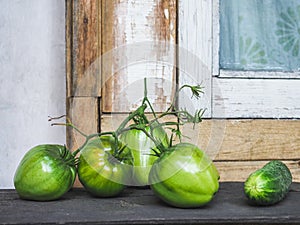 Branch of green tomatoes and cucumber lying on the railing of a village house