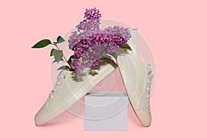A branch of lilac in sports sneakers. On a white square podium.