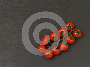 A branch of red cherry tomatoes on a dark slate background. Small and juicy vegetable is rich in vitamins and trace elements.