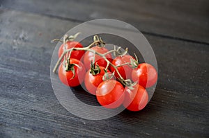 Branch of red cherry tomatoes isolated on black wooden background close up