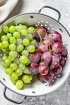 A branch of red and green grapes in a colander. Gray background. Top view