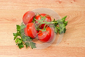 Branch of red tomatoes and parsley twigs on wooden surface