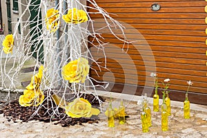 Branch with yellow roses and some yellow bottles with daisies on the floor on \