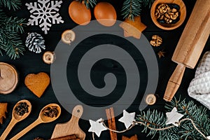 Branches of Christmas tree, gingerbread cookies, baking accessories and ingredients on black wooden table. Copy space