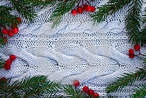 Branches of a Christmas tree and red berries on a white knitted sweater background. Top view. Copy space