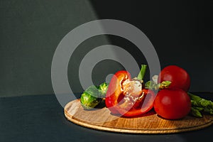 branches of fresh green asparagus, peppers, tomatoes and cucumbers on a wooden board, dark gray background, top view