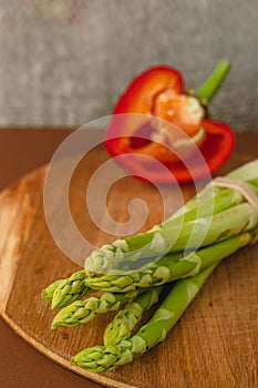 branches of fresh green asparagus on a wooden board, red big pepper on the background. brown background, top view. Basic