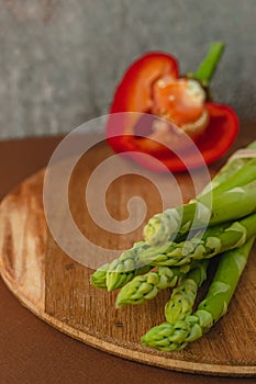 branches of fresh green asparagus on a wooden board, red big pepper on the background. brown background, top view. Basic