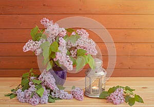 Branches of lilac in blue vase and lantern near on wooden table. Selective focus