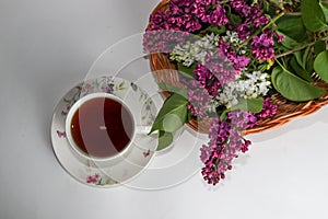 Branches of lilac and white lilac in a wicker basket and a cup of black tea with lilac flowers isolated on a white background