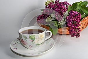 Branches of lilac and white lilac in a wicker basket and a cup of black tea with lilac flowers isolated on a white background