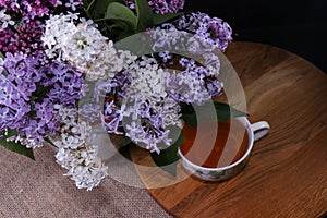 Branches of lilac and white lilac in a wicker basket and a cup of black tea with lilac flowers isolated on a white background