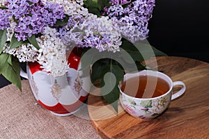 Branches of lilac and white lilac in a wicker basket and a cup of black tea with lilac flowers isolated on a white background