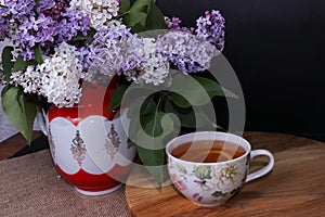 Branches of lilac and white lilac in a wicker basket and a cup of black tea with lilac flowers isolated on a white background