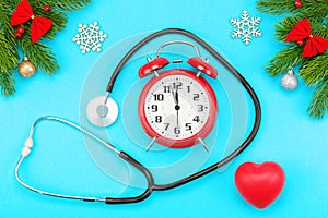 Branches of spruce, christmas toys, red heart with stethoscope and alarm clock with five minutes to twelve o`clock