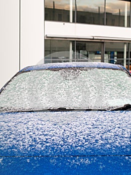 Brand new blue car covered with snow. Dealership in the background. Car sales in winter sales concept