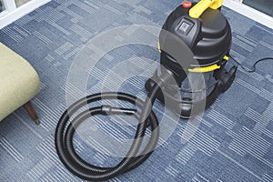 A brand new chrome upright vacuum cleaner placed on the carpeted flooring at the corner of an office space