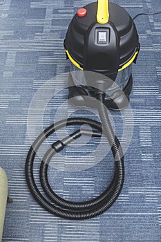 A brand new chrome upright vacuum cleaner placed on the carpeted flooring at the corner of an office space