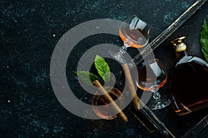 Brandy in glasses and cigars on a black stone table. Top view.