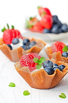 Brandy snaps baskets with soft cream cheese and berries on whit