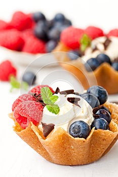 Brandy snaps baskets with soft cream cheese and berries on whit