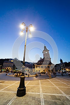 BRASOV, ROMANIA - AUGUST 1, 2017: People on central council square (Piata Sfatului) with town hall clock tower on summer evening.