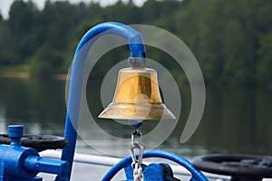 Brass bell on the foredeck of a ship against the background of a blurred wooded coast