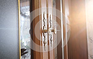 Brass door with glass inserts and handles with ornate escutcheons on a wooden cabinet , close up, authentic interior home photo