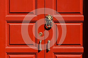 Brass lion head door knocker at the red wooden door.