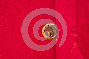 Brass lock on a blood red painted wooden door. Close up. Security, safety, safekeeping concept.