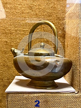 A brass tea pot with a handle sits on a table