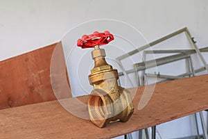 Brass valve with red knob in a factory plumber on wooden floor background