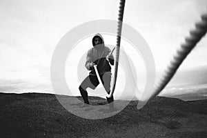 Brave athlete wearing sportswear doing intens workout using battle ropes on outdoor