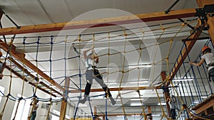 A brave boy climbs an obstacle in the form of a rope web in a rope park indoors
