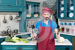 Brave chef with spoons in hands in red apron and red cap