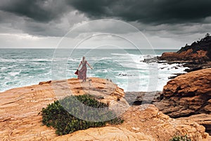 Brave female in long dress faces the dark storm by the ocean