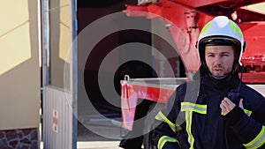 Brave firefighter man talking to walkie talkie with fire truck in background. Concept of saving lives, heroic profession