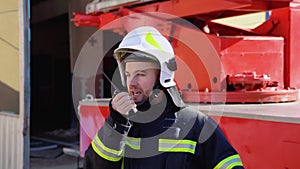 Brave firefighter man talking to walkie talkie with fire truck in background. Concept of saving lives, heroic profession