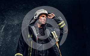 Brave fireman in a fire suit looking sideways and correcting the helmet with his hand