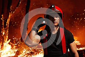 A brave fireman in helmet, holding a flashlight during the forest fire fight.