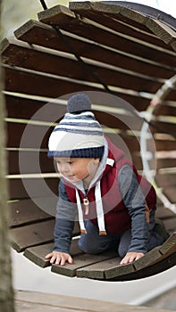 Brave little boy crawling along a wooden tunnel