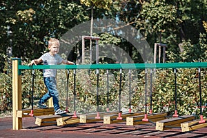 A brave little boy goes across the bridge of the monkeys in a city playground, against a green foliage background